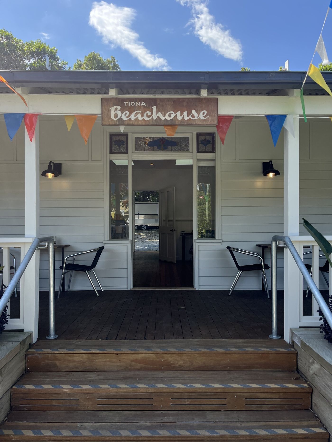 The Beach House Cafe entrance: white weatherboard, a timber sign reading Tiona Beachouse, bunting and barn lights