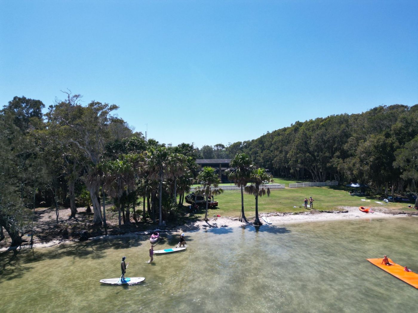 Wallis Lake from above, paddleboarders in the shallows off the park's lake beach