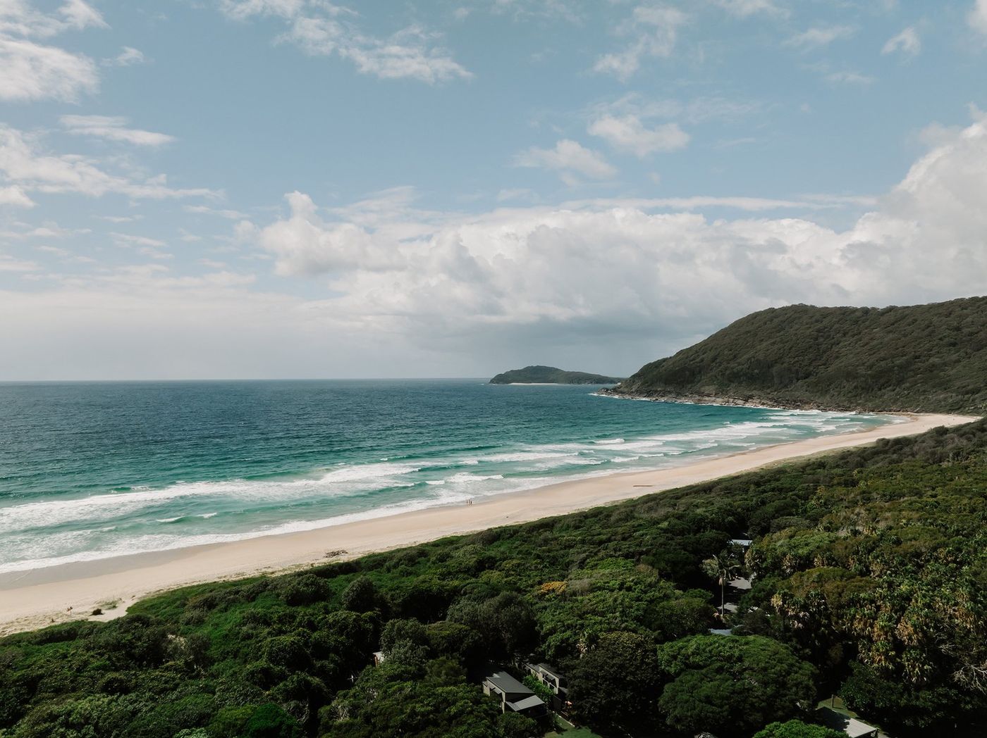 Seven Mile Beach curving away to the headland, with the park's trees in the foreground