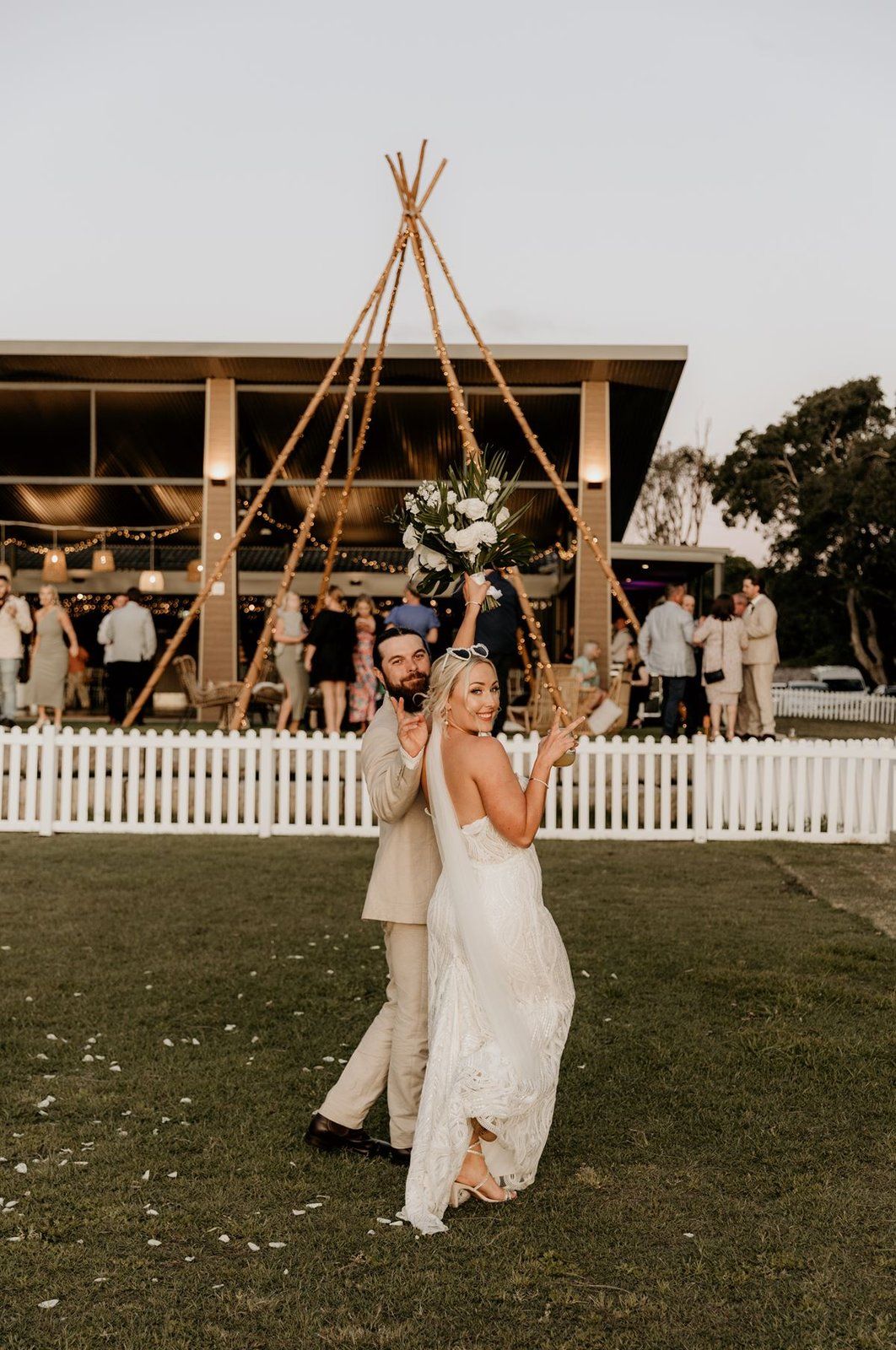 A couple on the lawn in front of the Palms Pavilion at dusk, fairy lights on the tipi behind them